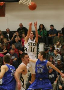 Stevensville’s Austin Lords lets fly with a long shot as teammate Jesse Sims blocks Blue Devils Jansen Jessop (20) and Andrew Leopold (32). The Yellowjackets topped Corvallis, 59-43. Jean Schurman photo